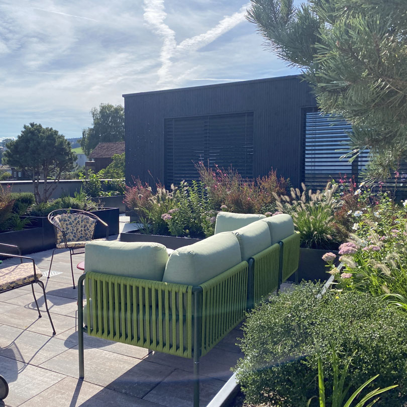 Grosszügige Terrasse mit üppig bepflanzten Hochbeeten  Grosszügige Terrasse mit Solitärbäumen und Bienenweiden bepflanzten Hochbeeten, farblich abgestimmte Lounge und passende Accessoires für entspannte Momente